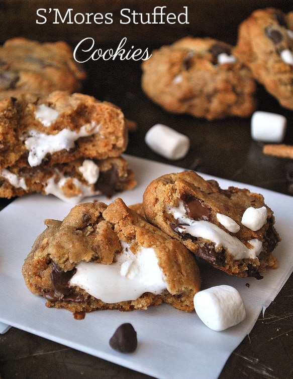 S'mores Cookies showing off gooey marshmallow filling close up with marshmallows, graham cracker,s and chocolate chips scattered around