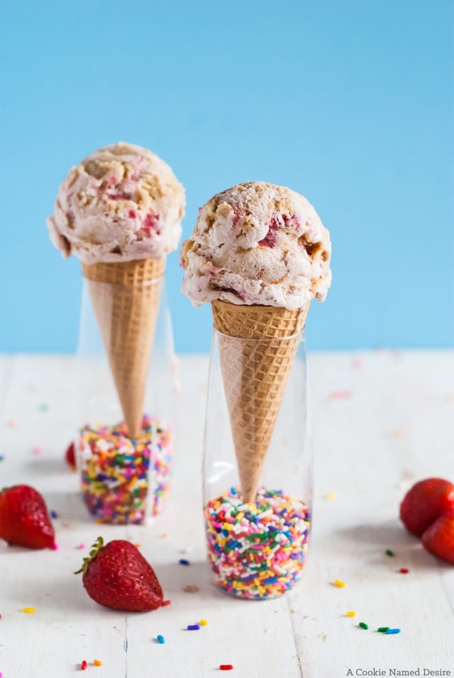 two ice cream cones with ice cream surrounded by strawberries and sprinkles