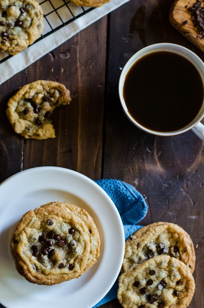 overhead cookies on a plate and scattered on a brown table next to mug of coffee