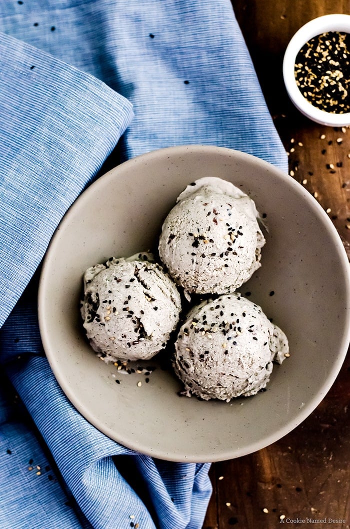 Three scoops of black sesame ice cream in a bowl garnished with more seeds