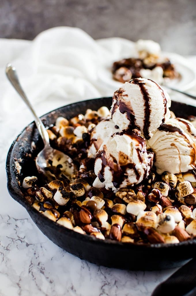 Pan of rocky road brownies with nuts and toasted marshmallows topped with ice cream