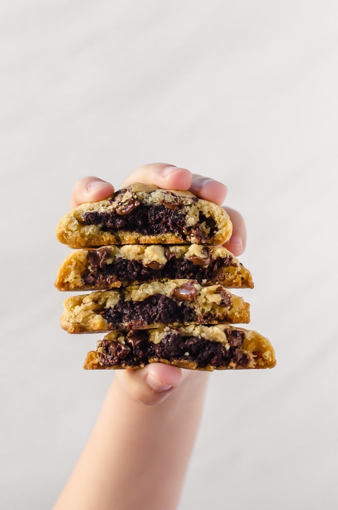 person holding brownie stuffed chocolate chip cookies with the filling showing