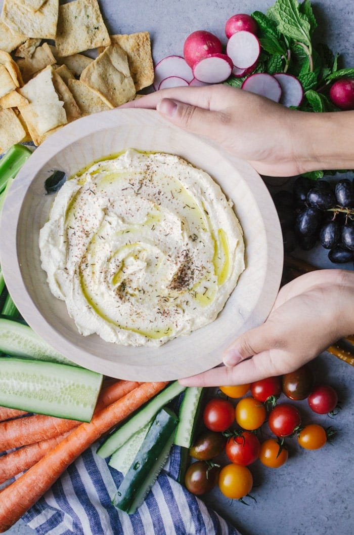 Hands placing bowl of dip on table by fresh fruits and vegetables