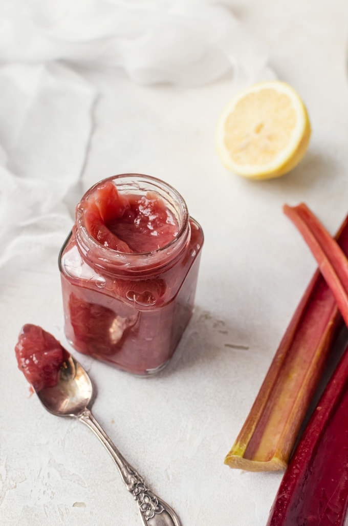 looking into jar filled with jam sitting next to spoonful of jam and rhubarb stalks and sliced lemons