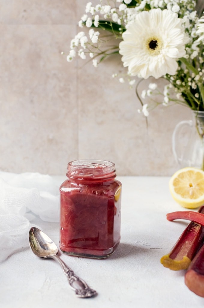 Straight on shot of jar full of rhubarb jam nex tto stalks of rhubarb and sliced lemon