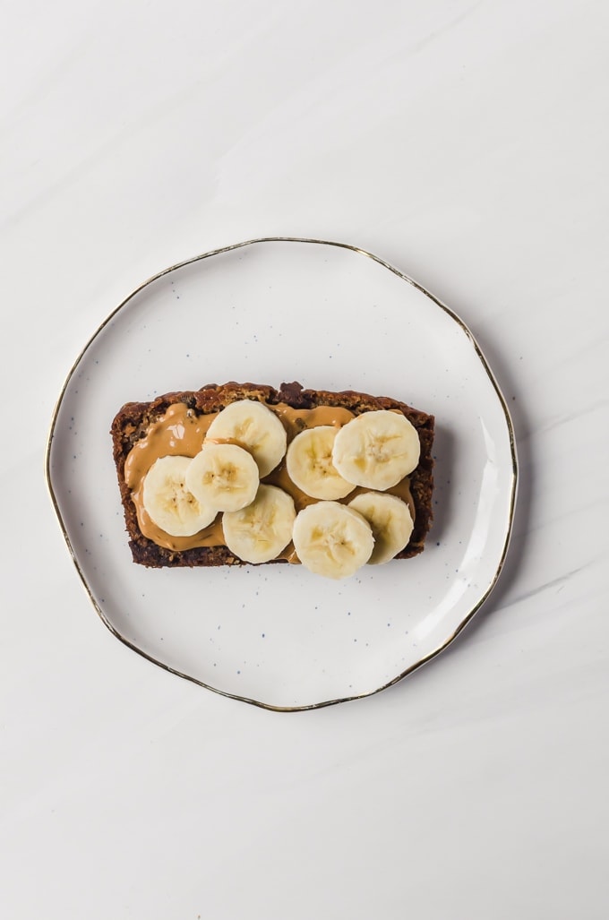 Slice of brown butter banana bread with peanut butter and sliced bananas on a plate