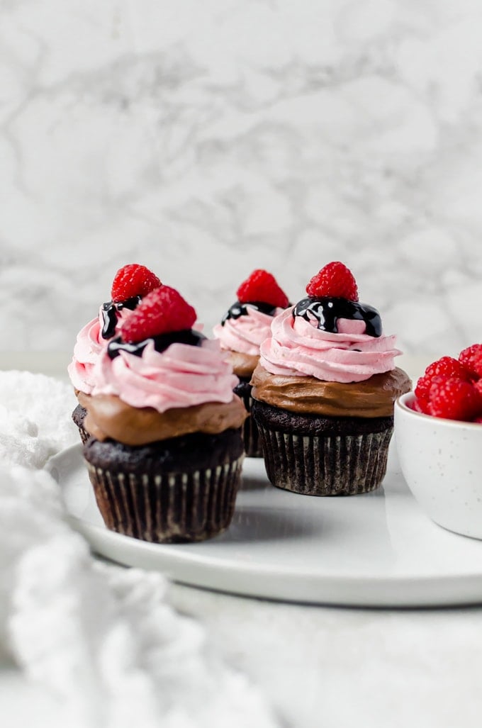 plate of nutella chocolate cupcakes with raspberry whipped cream and a bowl of raspberries