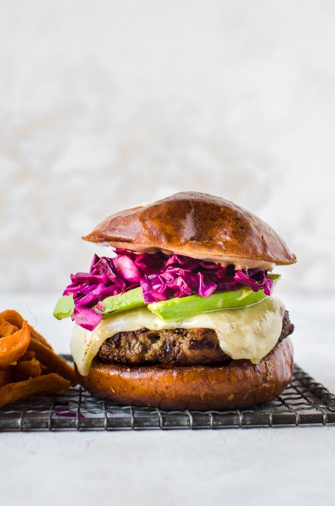 close up juicy turkey burger topped with cheddar cheese, sliced avocado, red cabbage all on a pretzel bun and served with sweet potato fries