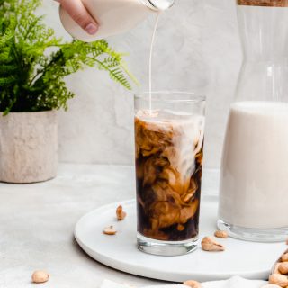 creamy cashew milk poured into glass of iced coffee