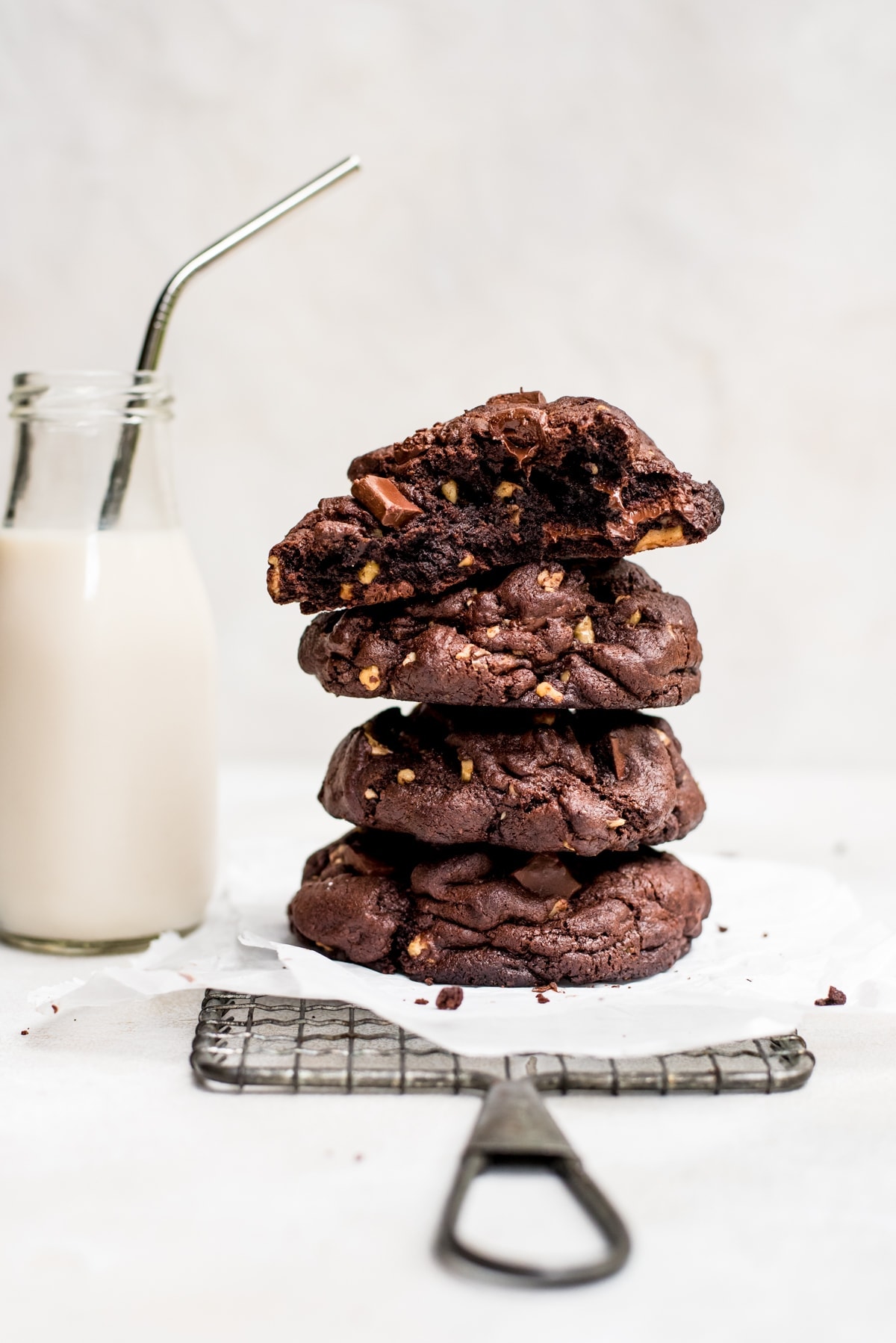 stacked giant double chocolate cookies on wire rack with glass of milk