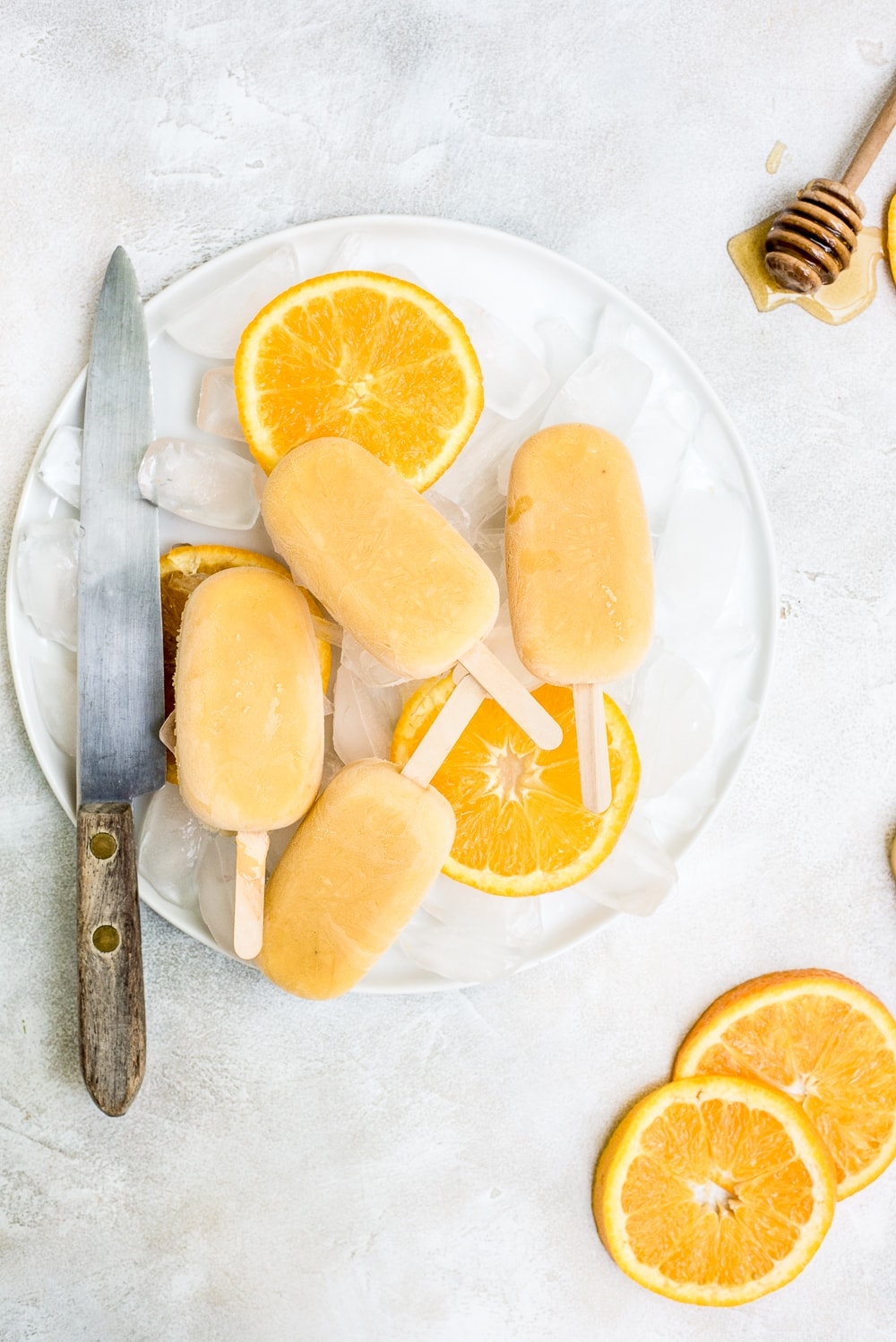 orange creamsicle popsicles on plate with ice and sliced oranges