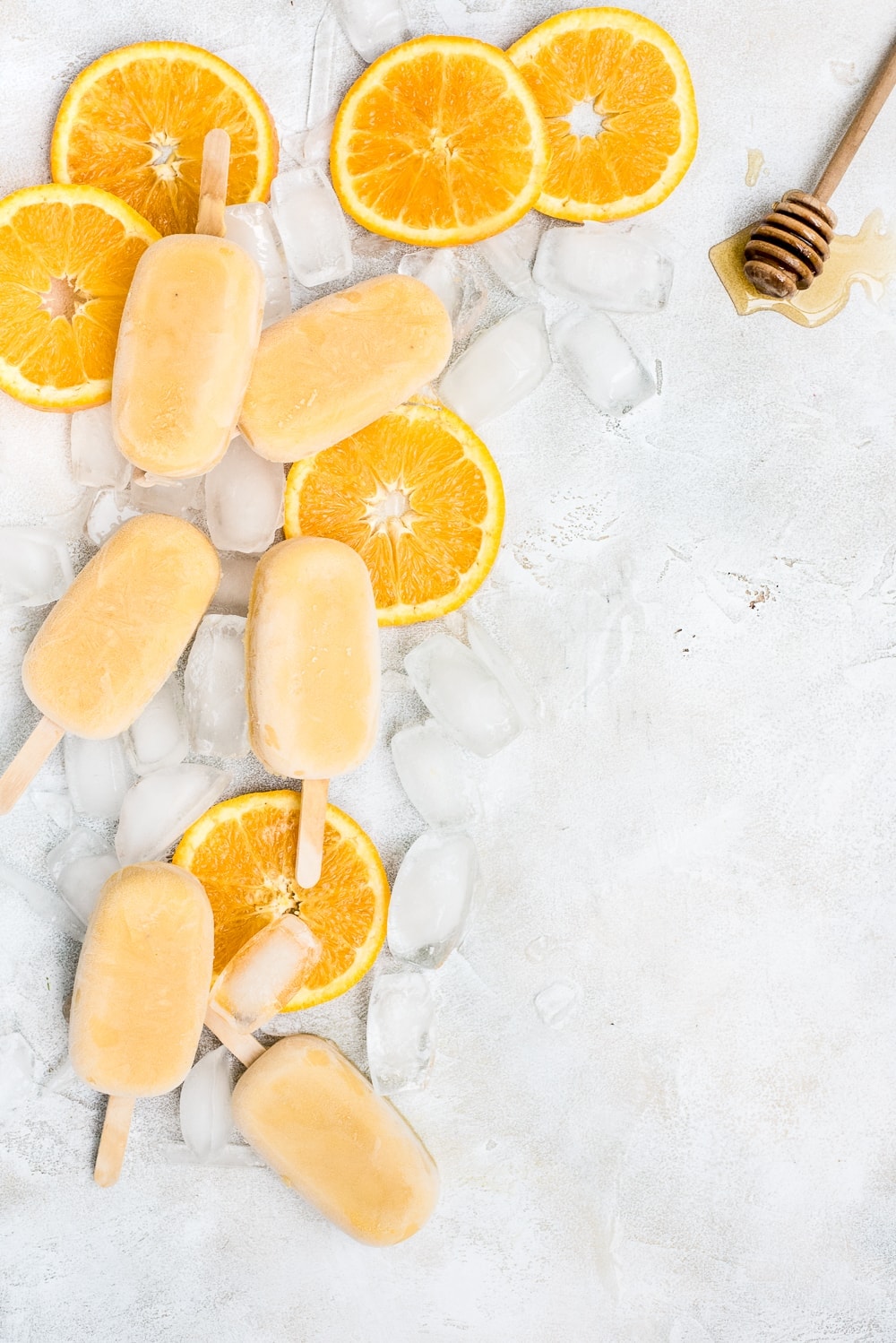 orange creamsicle popsicles scattered on table with ice and oranges