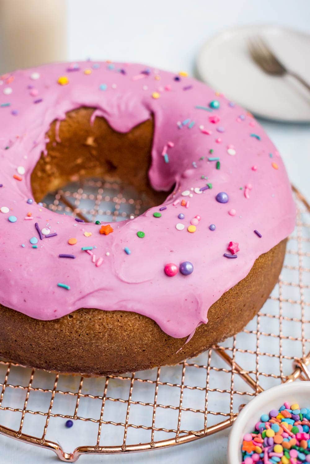 donut cake with punk frosting and sprinkles on copper wire rack