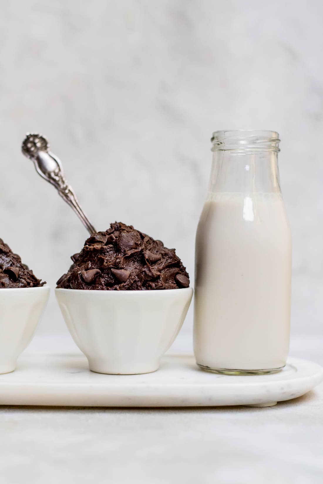 edible brownie batter in white bowl next to milk bottle