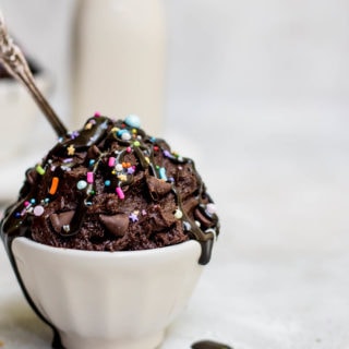edible brownie batter in bowl topped with fudge sauce and sprinkles