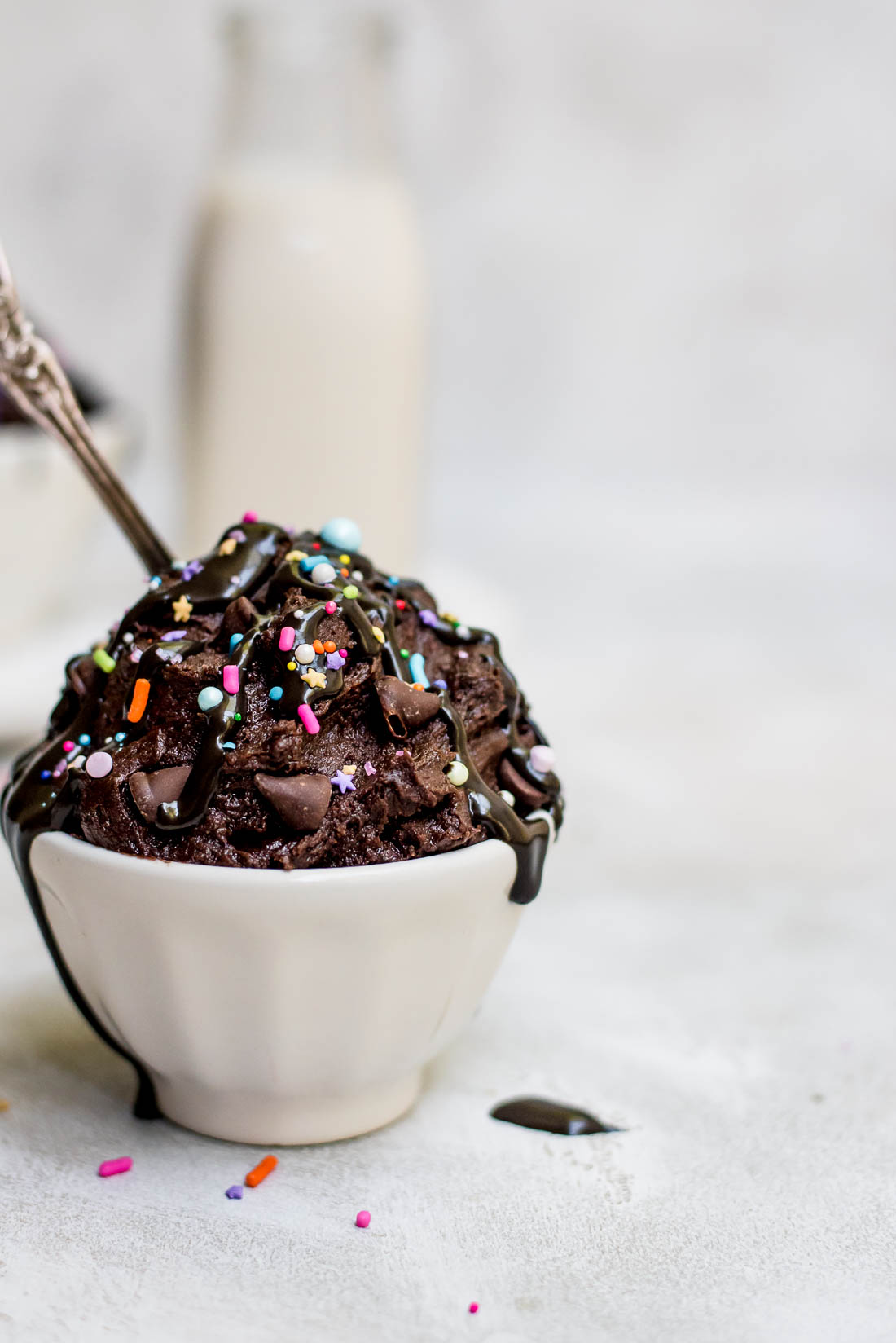 edible brownie batter in bowl topped with fudge sauce and sprinkles