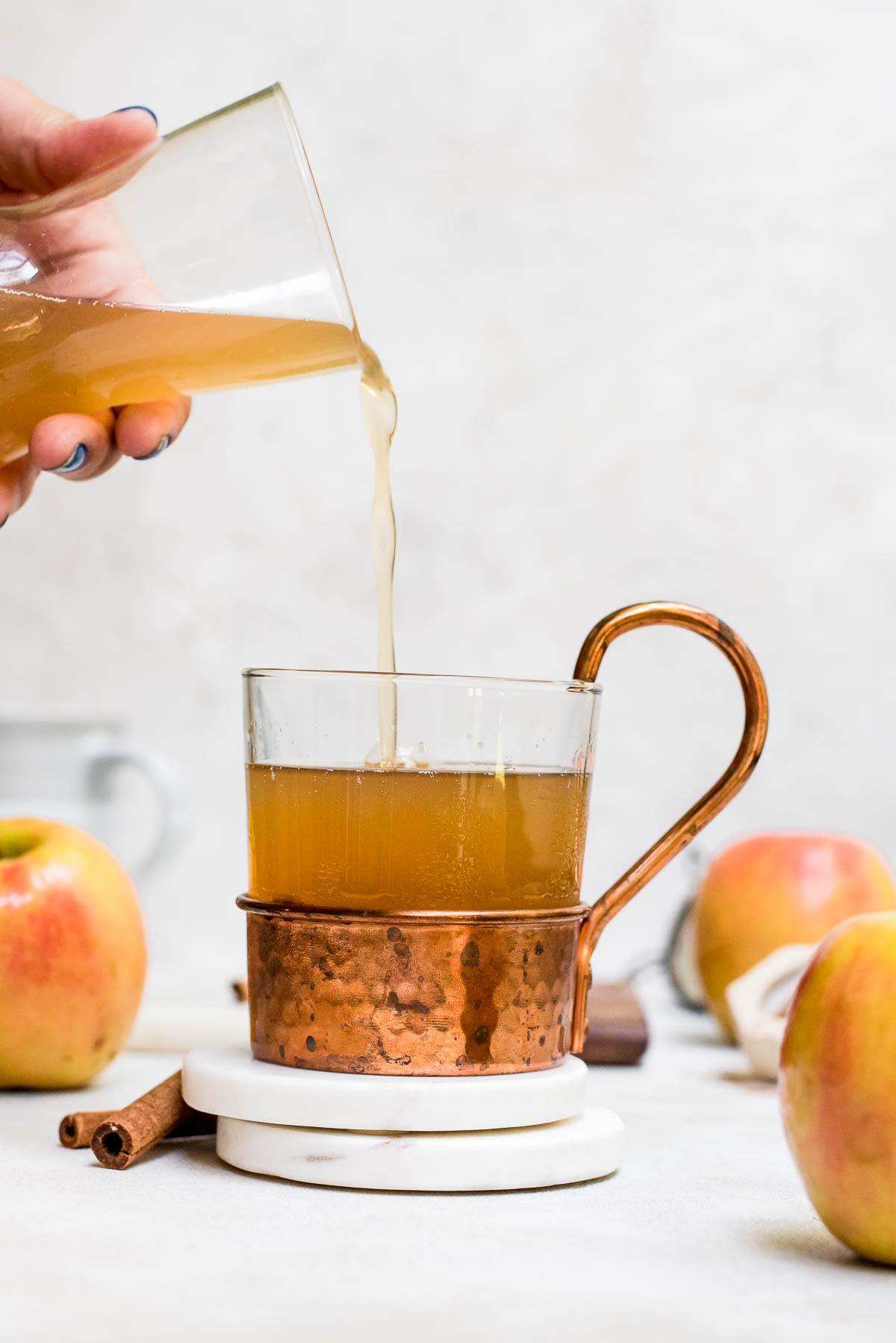 warm homemade apple cider in a glass and copper mug on white marble coaster