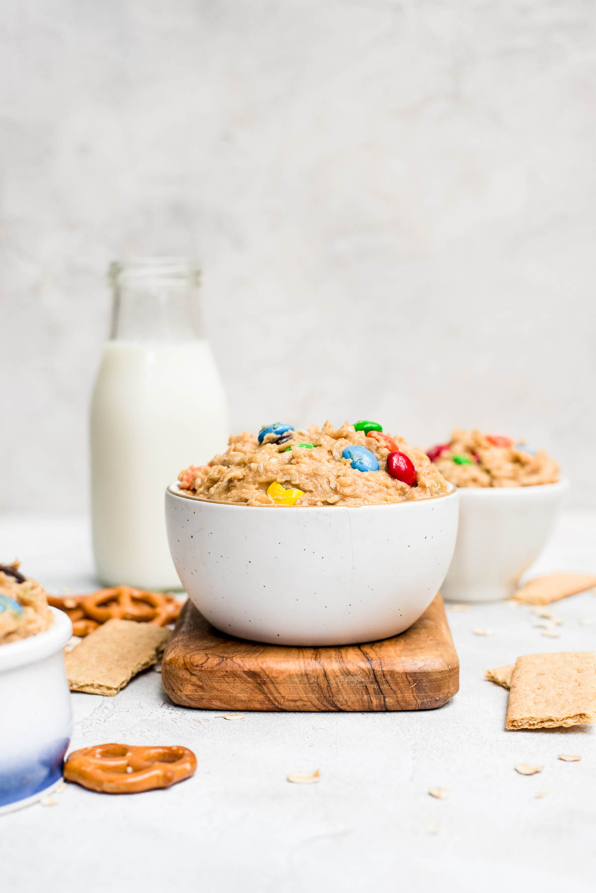 monster cookie dough dip in small bowl on cutting board with ingredients and milk