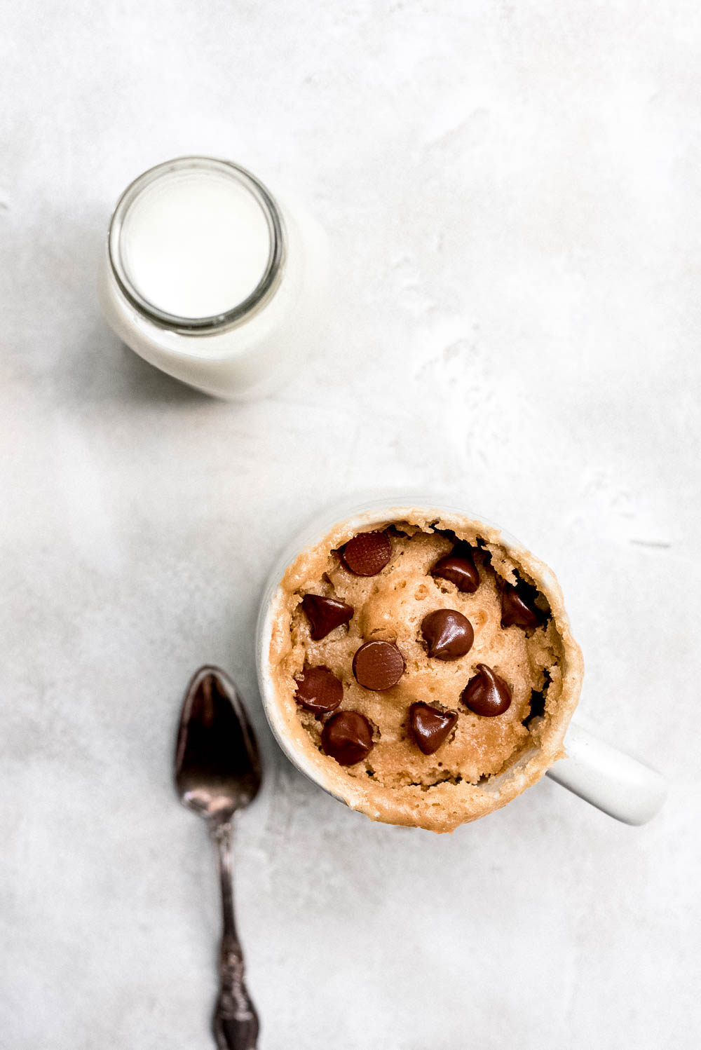 Overhead peanut butter mug cake in large white mug with silver spoon