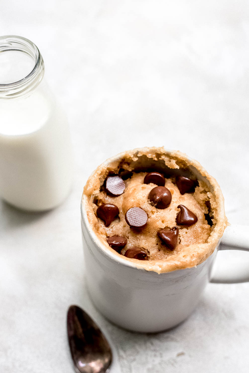 close up peanut butter mug cake in large mug milk in background