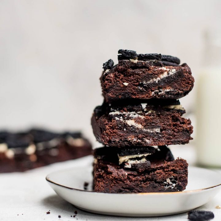 oreo brownies stacked on white plate with milk jug in background