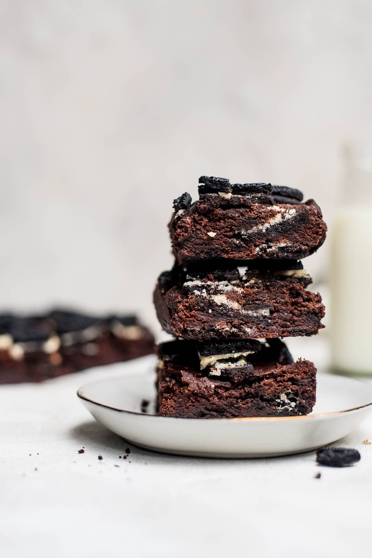 oreo brownies stacked on white plate with milk jug in background