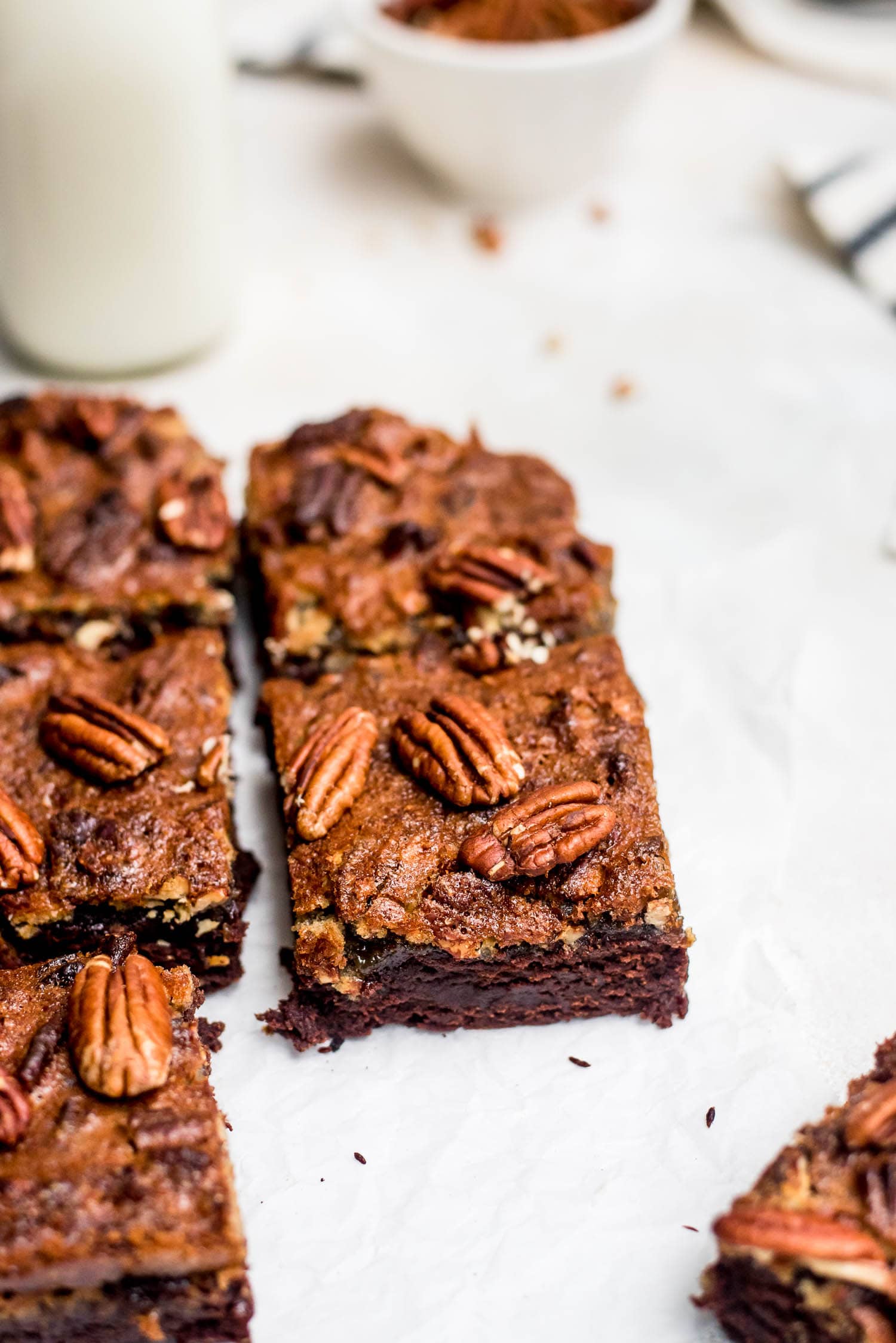 sliced brownies on parchment with pecans and glass of milk