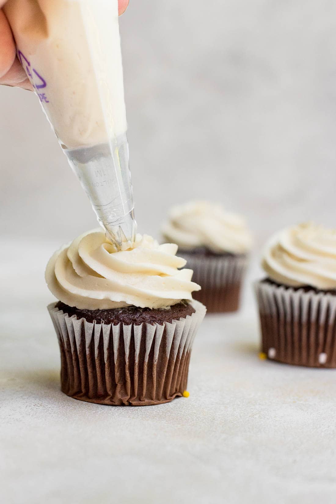frosting being piped on cupcake
