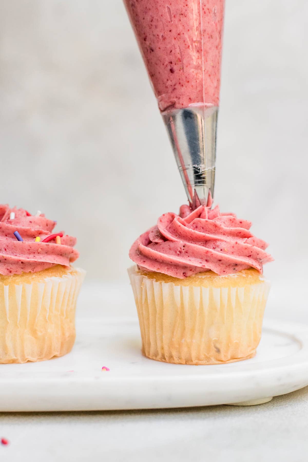 cupcakes being pipped with strawberry buttercream frosting