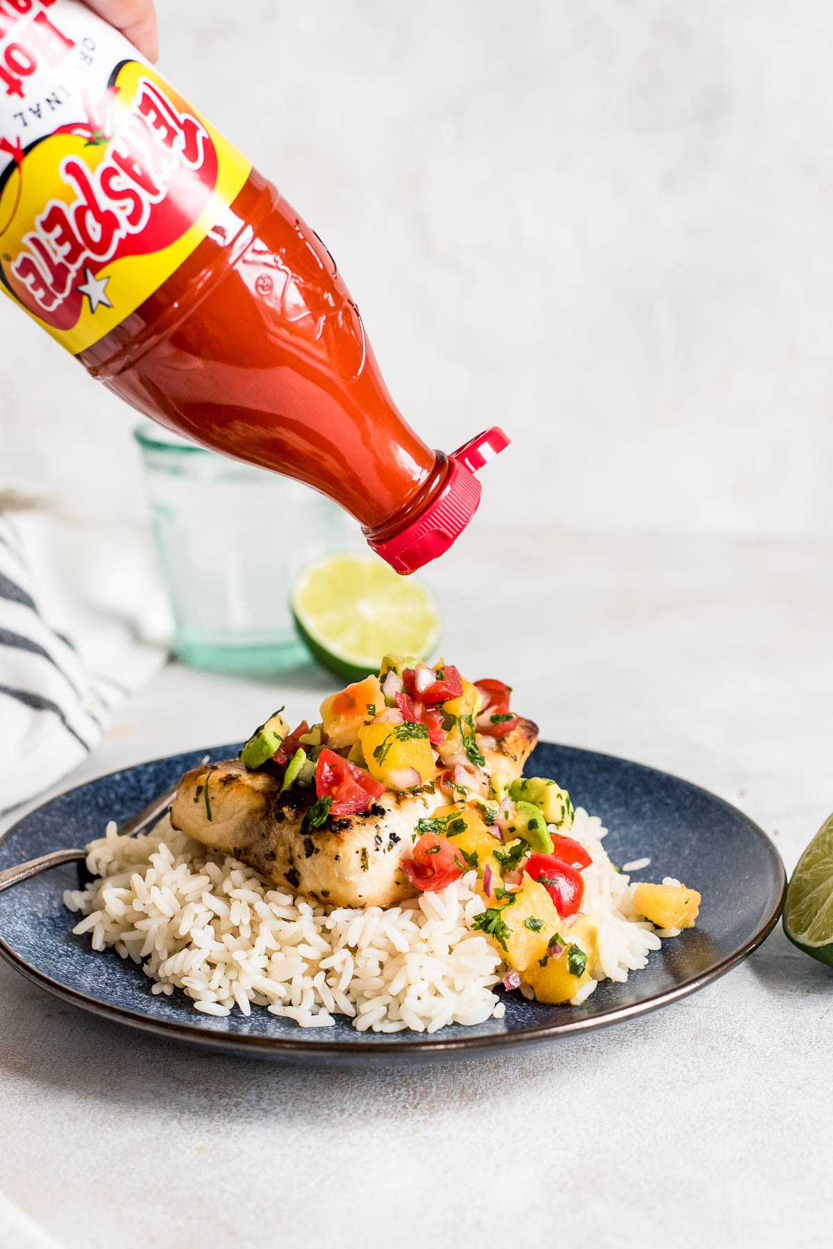 Texas Pete hot sauce being added to swordfish that is topped with salsa and on bed of rice on blue plate