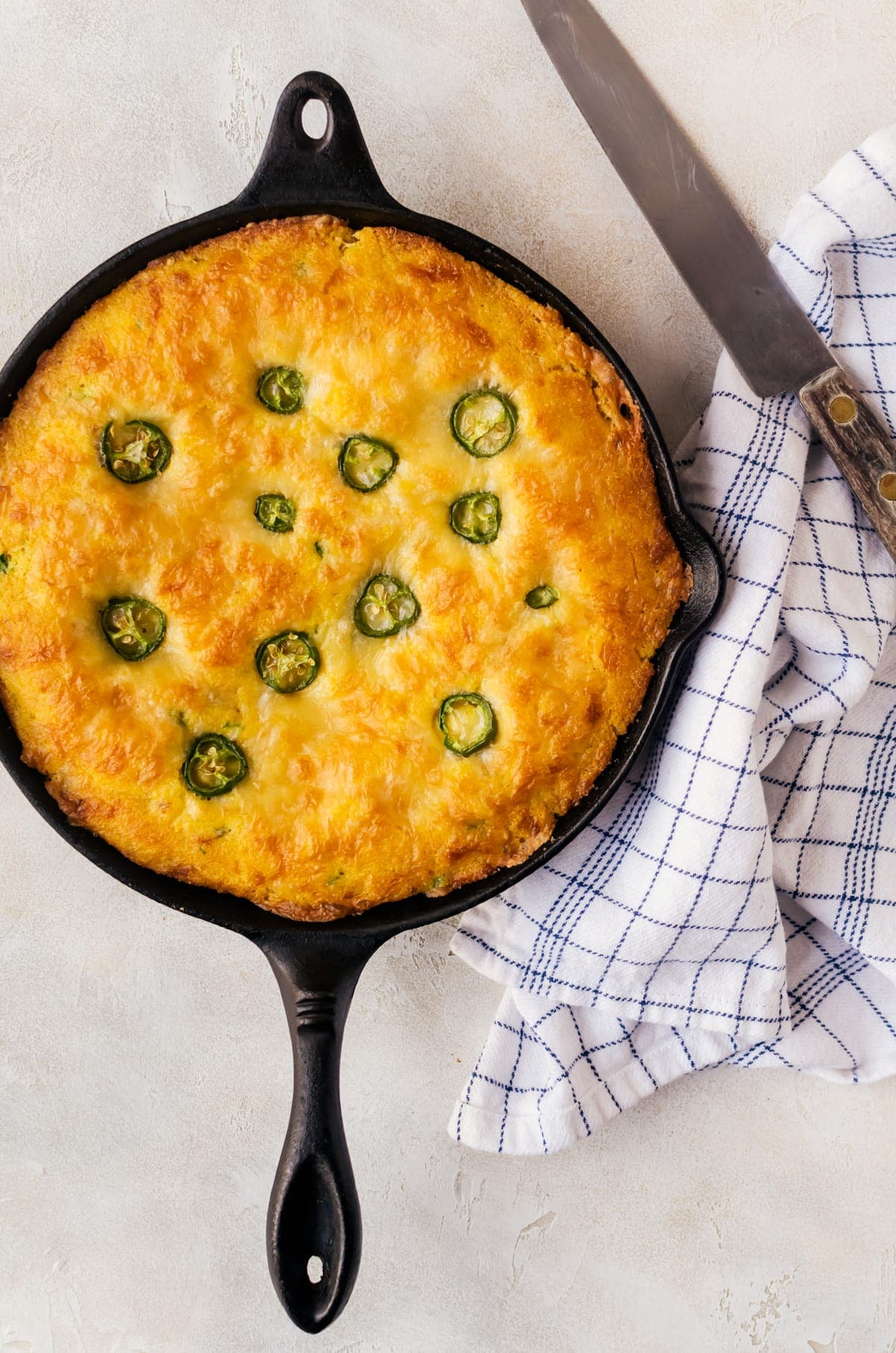 cheddar jalapeno cornbread in skillet on table with kitchen towel