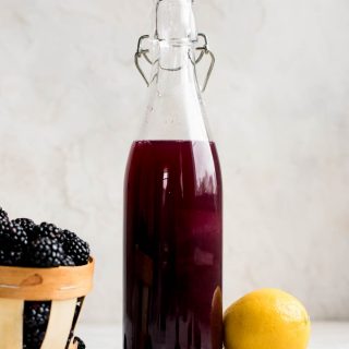 blackberry syrup in bottle next to blackberries and lemon