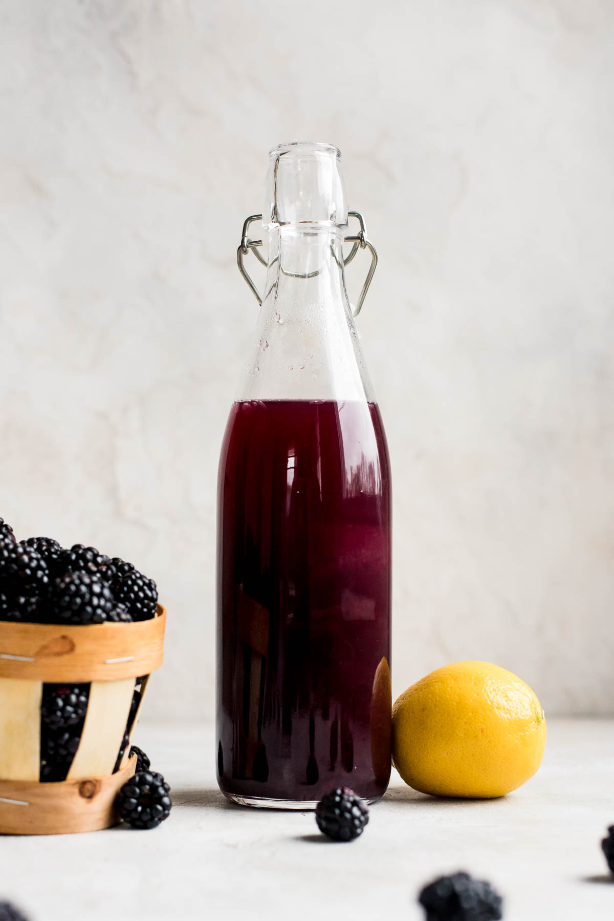 blackberry syrup in bottle next to blackberries and lemon