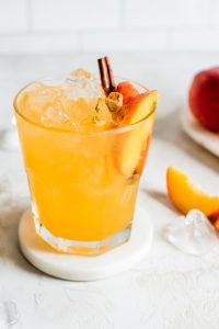 close up shot of moonshine with peach slice and cinnamon stick garnish