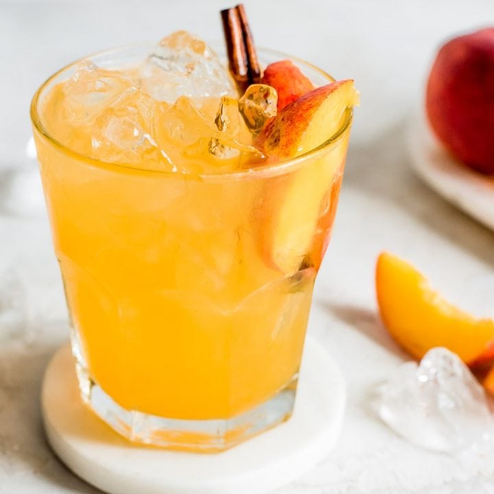 close up shot of moonshine with peach slice and cinnamon stick garnish