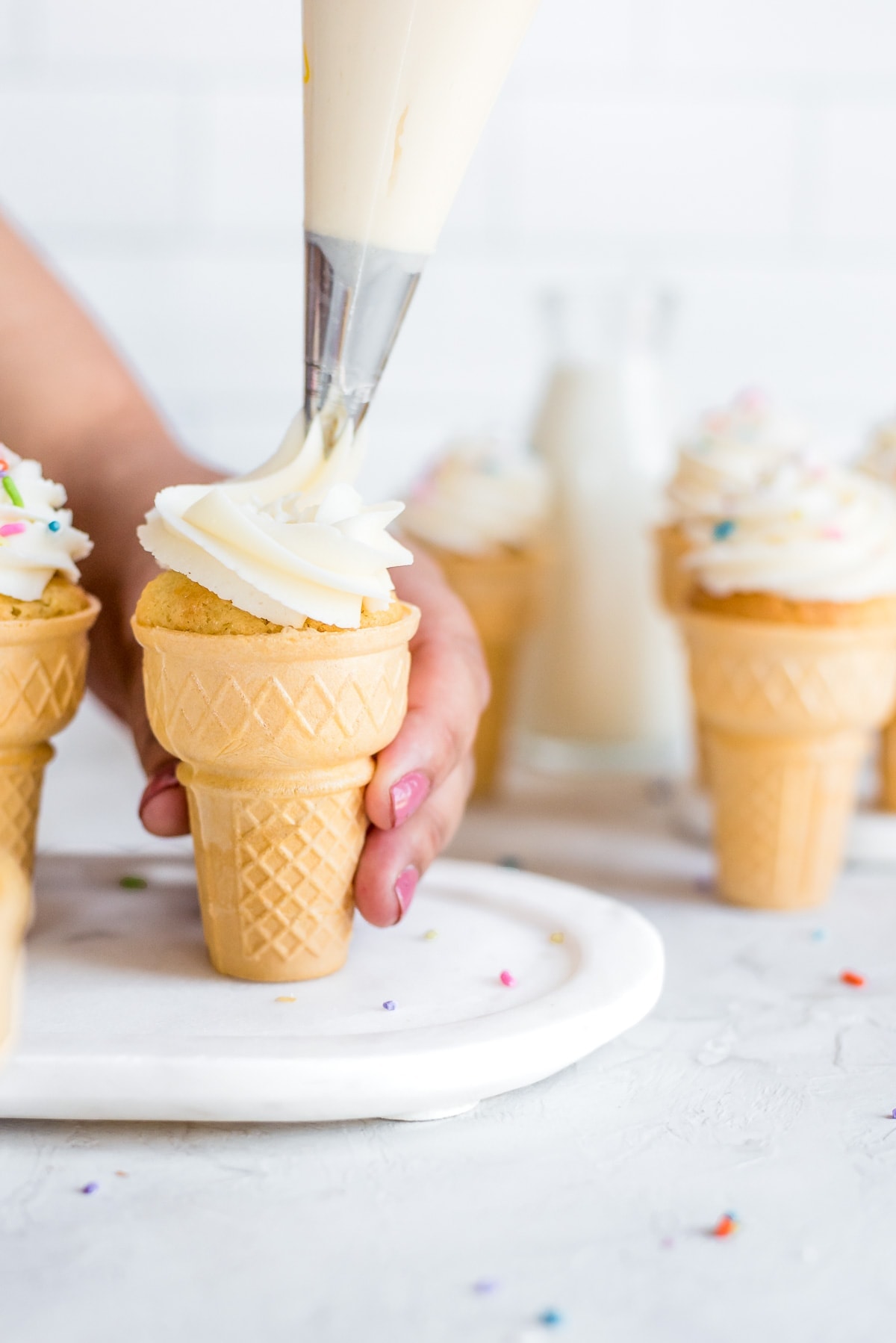 cupcakes in ice cream cone being topped with frosting