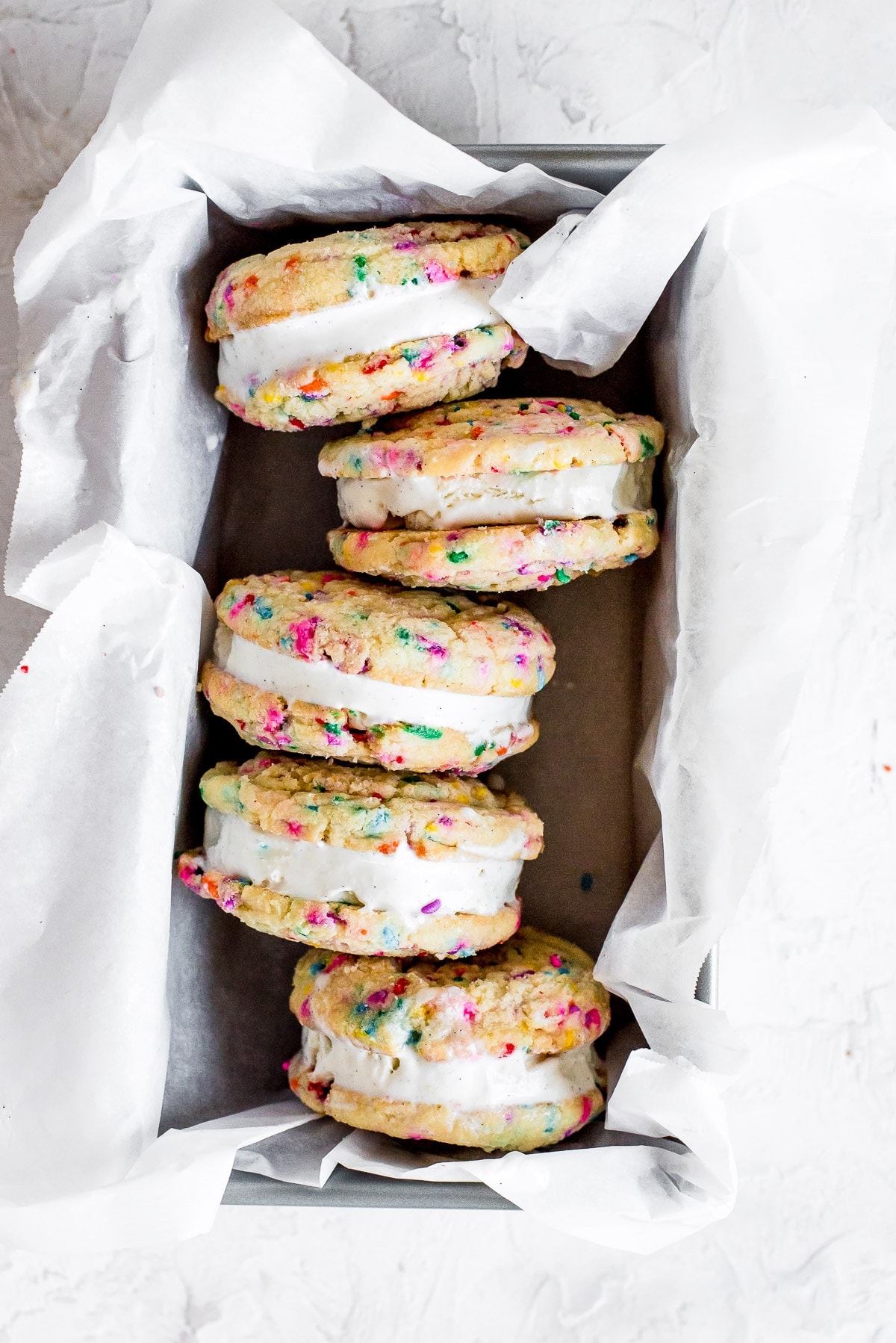 sugar cookies sandwiching ice cream in pan with parchment paper on bottom