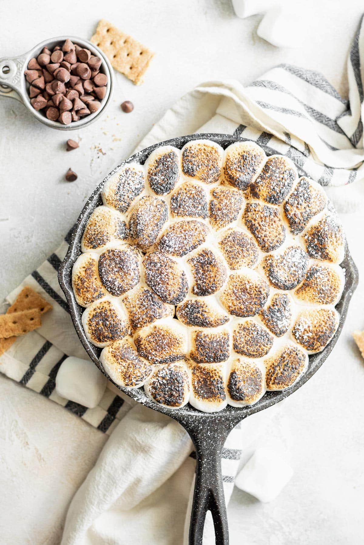 dip dusted in powdered sugar in skillet on table with chocolate and marshmallows scattered around