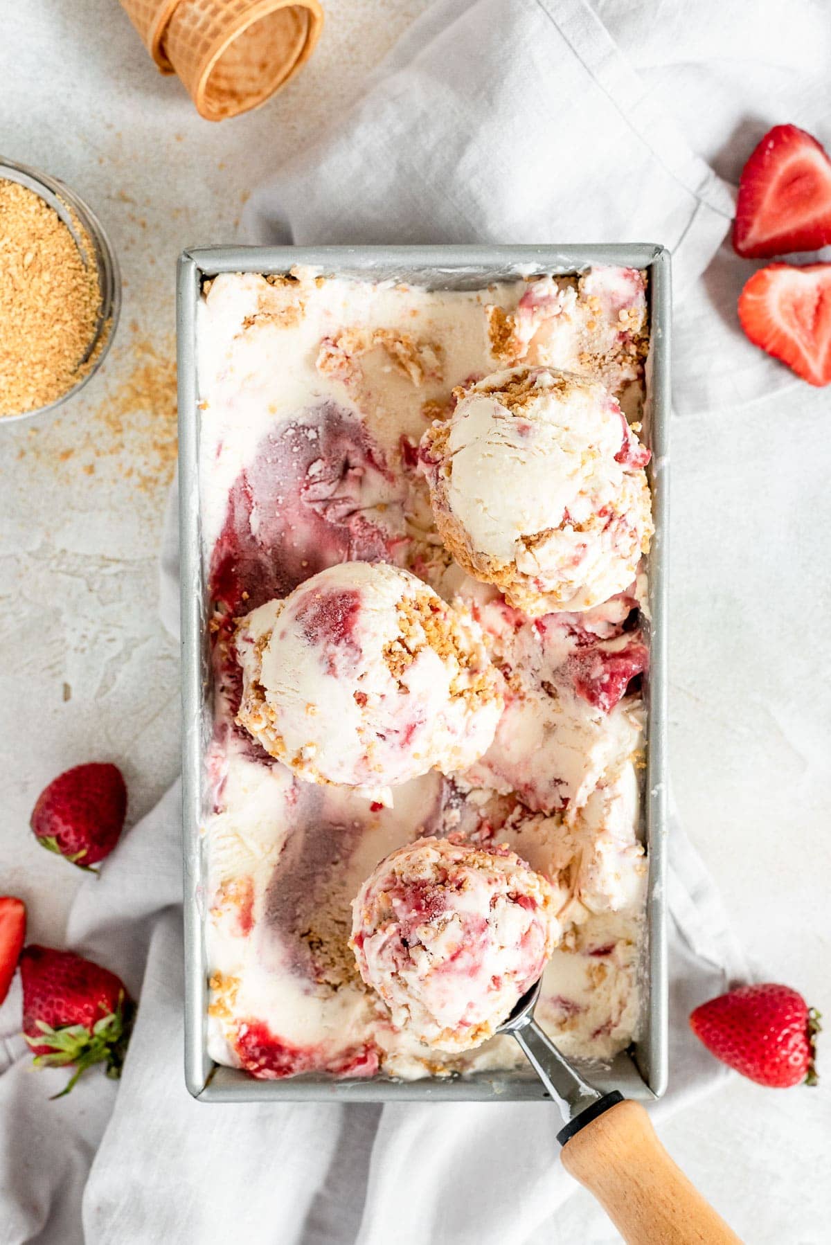 overhead ice cream in container being scooped, surrounded by strawberries and ice cream cone