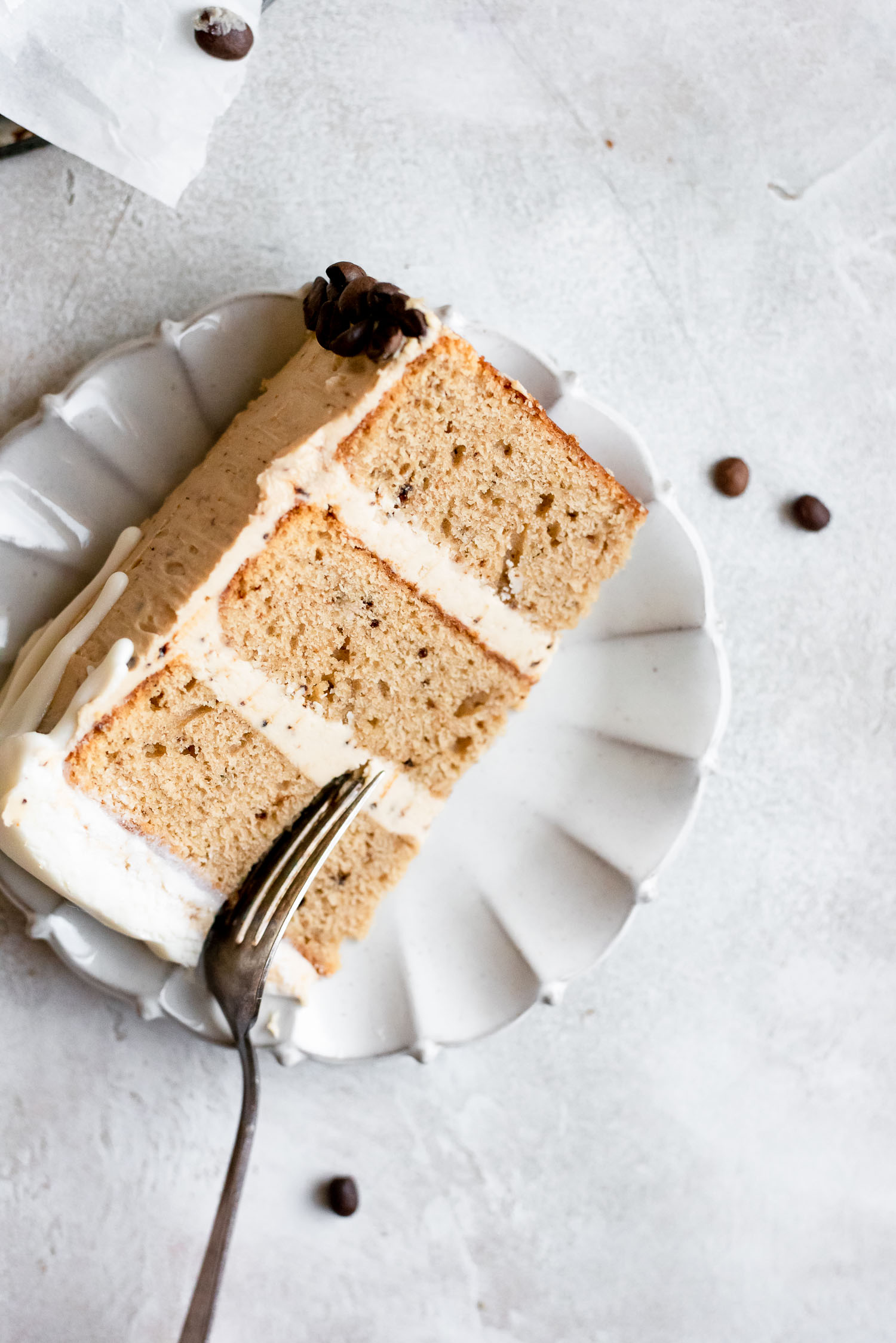 white chocolate mocha cake slice on white ruffle-rimmed plate with fork cutting into cake