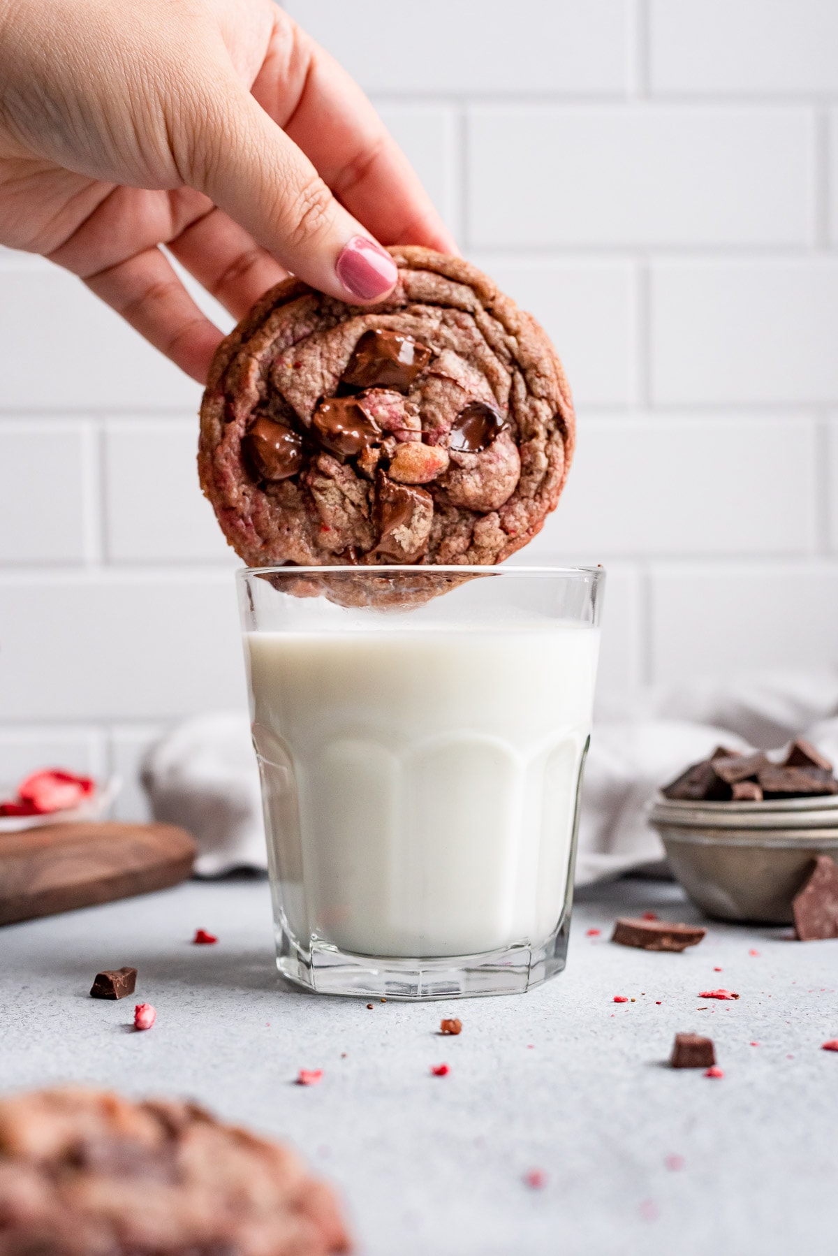 hand dunking strawberry chocolate chip cookie in glass of milk