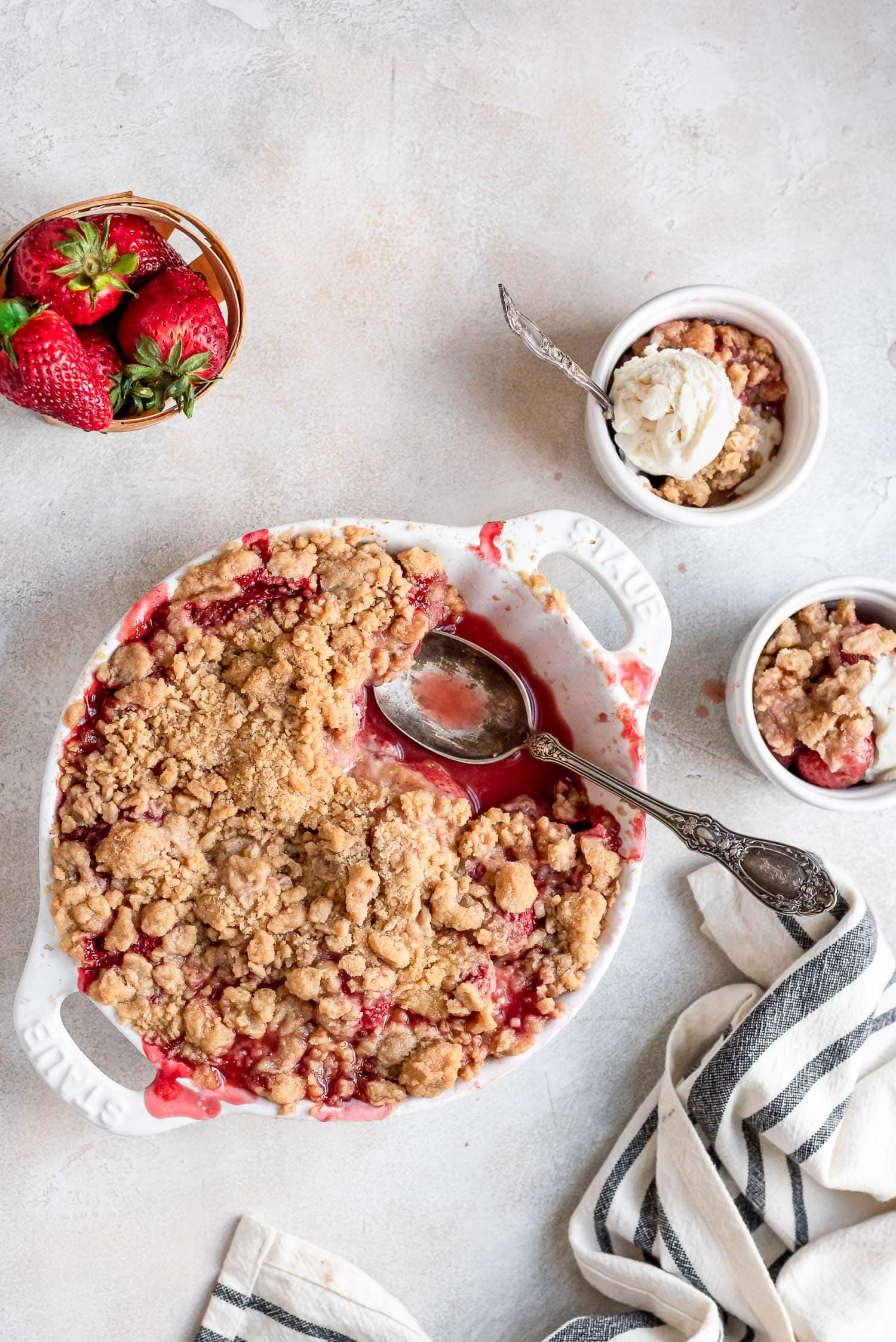 strawberry crumble in pan next to bowls and fresh berries
