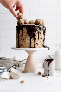 hand placing cookie dough truffle on cake