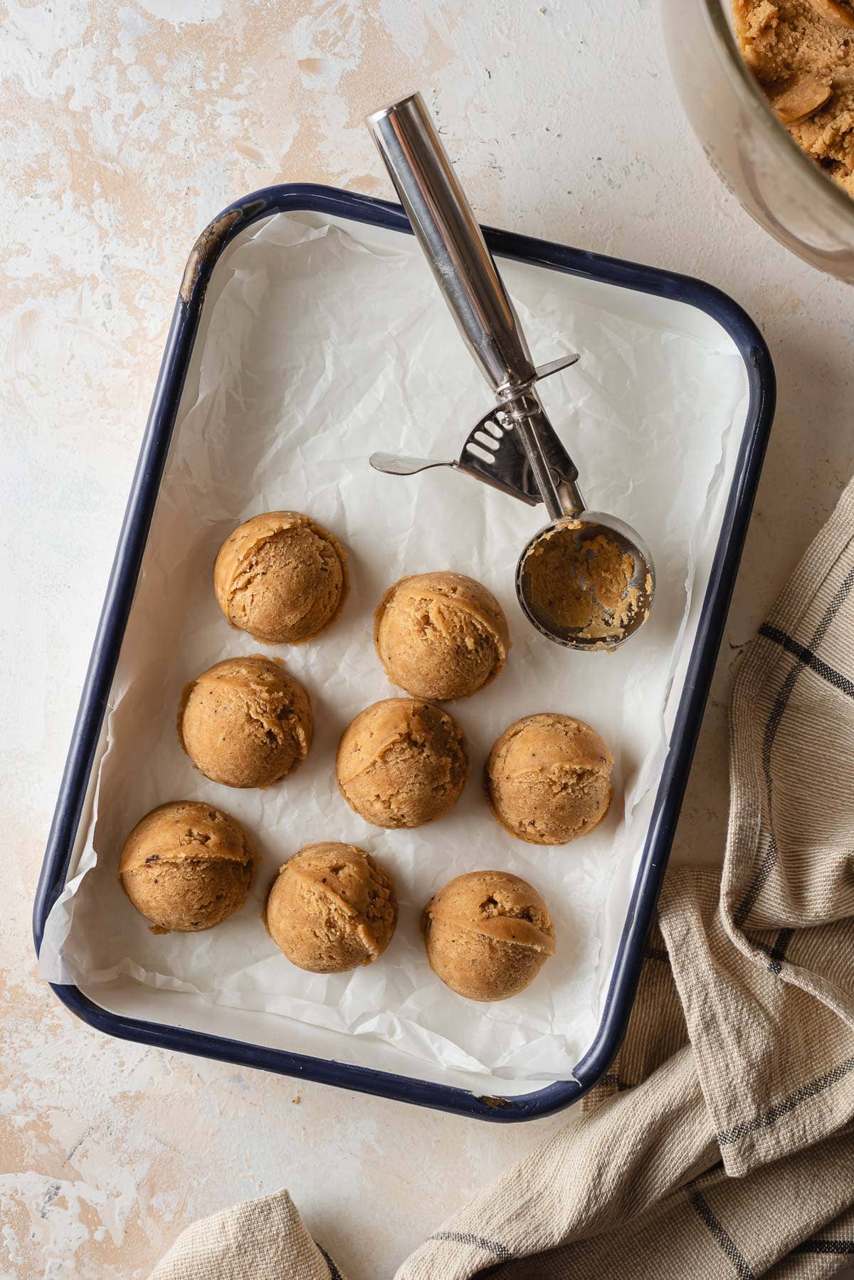 chocolate chipless cookie dough being portioned out on baking sheet lined with parchment paper